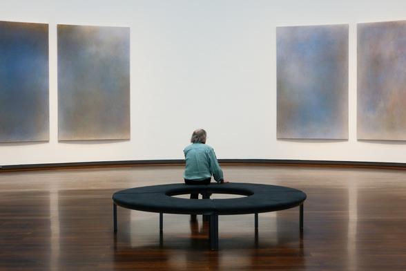 A man sitting on a bank, abstract paintings on the wall