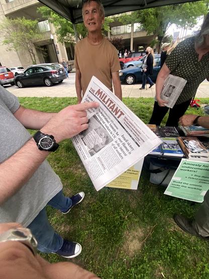Man points to "THE MILITANT" newspaper held in his other hand.