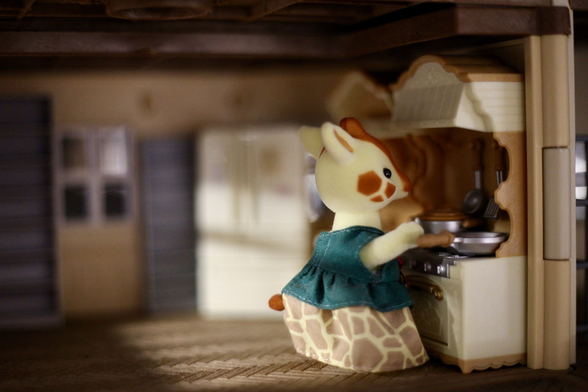 a photo of the interior of a sylvanian families dollhouse kitchen, with a giraffe mother cooking food. the light shines in from the side, giving it a nice cozy and warm feeling and look