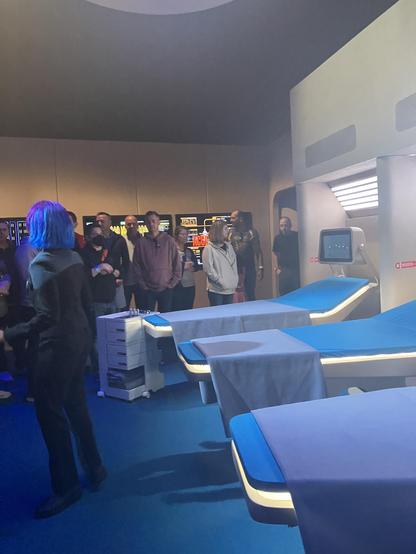 Sick Bay from Star Trek: The Next Generation recreated by Universal Studios Hollywood. Three blue beds are visible along with an actor in a Star Trek Uniform. Several people are lined up near a wall
