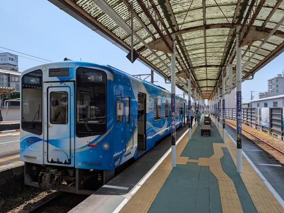 Photo of a single car train at a small outdoor train station with a curved translucent fiberglass awning over the platform.