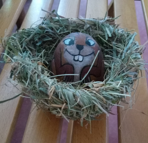 Auf einem Holzrost steht ein Grastopf, und aus dem Grastopf guckt ein eiförmig er Holzhase.