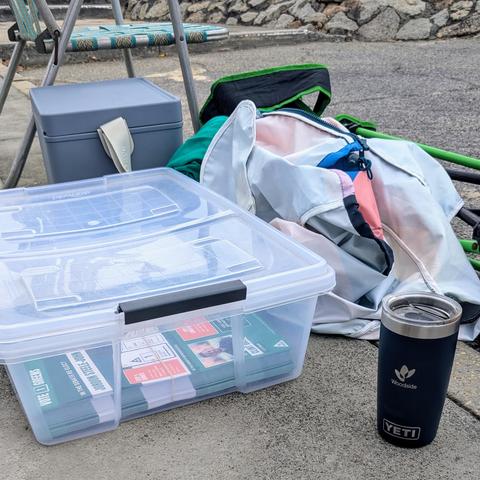 A box of How to Vote flyers for The Greens in a West Australian electorate, with incumbent Senator Jordon Steele-John's name visible. It is juxtaposed against a Yeti Rambler cup engraved with the logo for Woodside Petroleum.