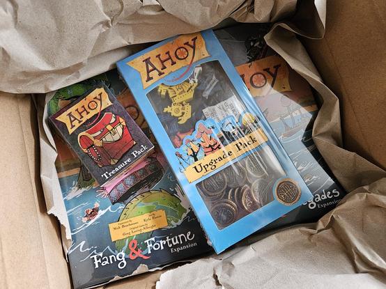 Blick in einen gerade geöffneten Versandkarton. Darin vier unterschiedlich große Boxen, die alle unterschiedliche Erweiterungen für das Brettspiel "Ahoy" enthalten.