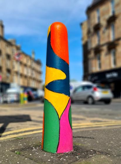 A concrete bollard on a Glasgow Street painted with blocks of bright colours.