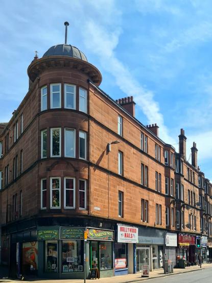 A red sandstone corner tenement with a domed roof and finial.
