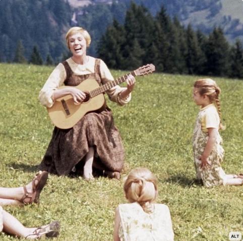 Maria from The Sound of Music in the iconic scene in a sunny mountain meadow, sitting with an acoustic guitar in hand, singing to the children.