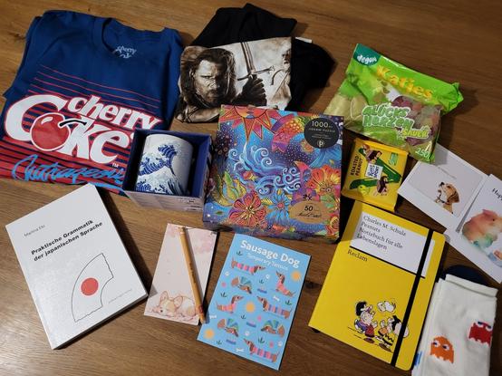 Various nerdy birthday presents with snoppy, sausage dogs, corgis, colorful puzzles, aragorn tshirt, cherry coke tshirt, japanese grammar