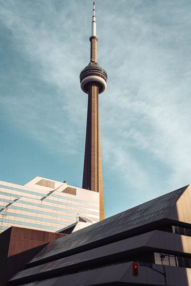 CN Tower viewed from Toronto’s Entertainment District during golden hour, with warm sunlight illuminating the tower against a clear sky.