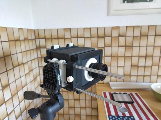 Photo of a home made 4x5" plate camera set up on a tripod. It's made from 3D printed parts and black foam core board, mounted onto some 8mm linear shafts from a 3D printer to allow for focusing.