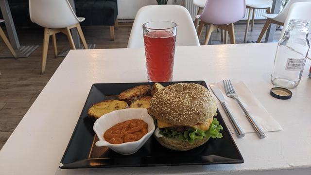 A plate with a burger, potato wedges and some dip along with a glass with a red drink.