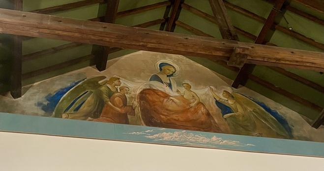 Au dessus de l’écran, fresque contemporaine d’une Vierge à l’Enfant entourée d’anges. Poutres apparentes de la salle.