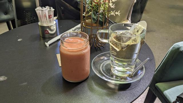A glass with smoothie and a cup of tea in a café.