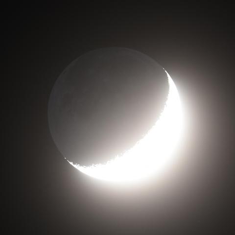 Die überbelichtete vier Tage alte Mondsichel am dunklen Nachthimmel. Der dunkle Teil des Mondes wird im aschfahlen Licht schwach sichtbar