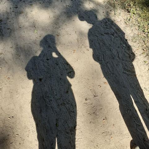A picture made outdoors. The shadows of a man and a woman are visible on sand.
