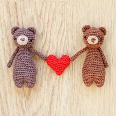 A picture of two small crocheted brown bears holding a red amigurumi heart together.