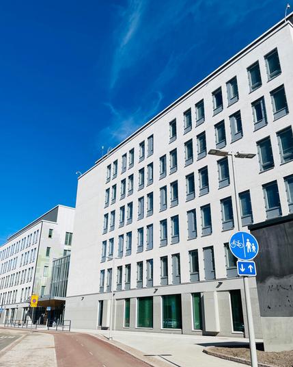 Modern building facade with large windows under a clear blue sky, alongside a bike and pedestrian pathway sign.
