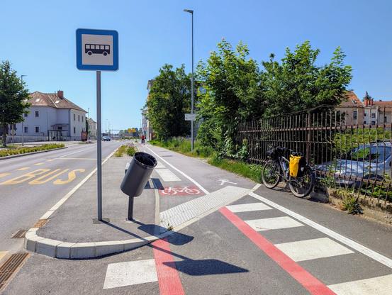 A dedicated cycling lane running next to a pedestrian path on the sidewalk. To the left of the cycling lane there is a trash can inclined in such a way that a cyclist can easily throw some small trash while cycling.
