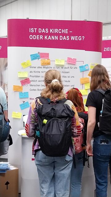 Menschen vor einer Wand mit Gedanken zum Thema Kirche. Die Frage "Ist das Kirche oder kann das weg" gilt es individuell zu beantworten.