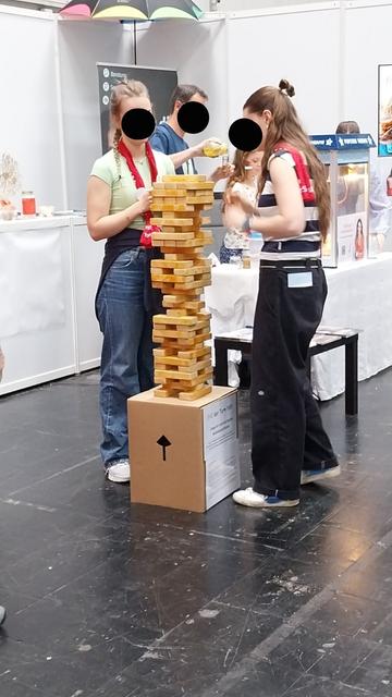 Zusammenarbeit im Team beim Abbau eines Turms aus Holzklötzen stärkt den Teamspirit zweier junger Besucherinnen.