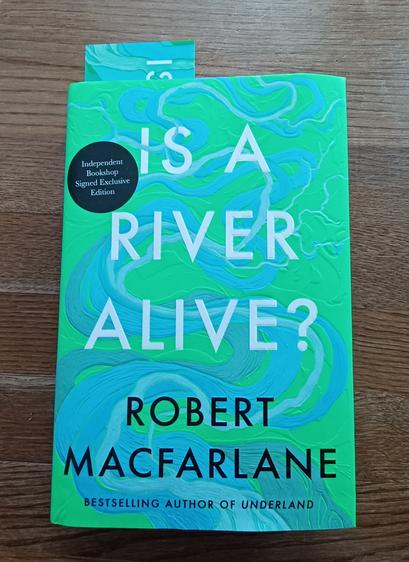 Book cover of #Is a River Alive by Robert MacFarlane in bright swirling Green and turquoise. There is a small black decal top left which says "Independent Bookshop Signed Exclusive Edition"