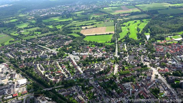 An aerial photo of a city, Herten Westerholt, from above. Some woods and agricultural fields can be seen in the distance.