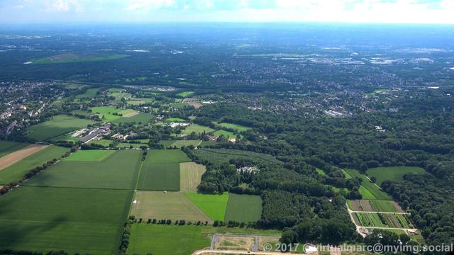 An aerial photo of agricultural fields and woods, some cities can be seen in the distance.