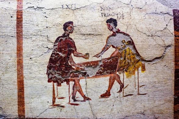 a cracked wall painting in the sketchy dark Roman style of two seated gamblers with a table between them resting on their knees