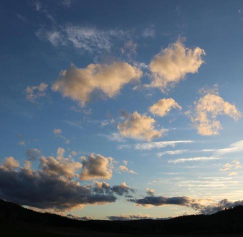 Photograph of a blue sky at sunrise, showing different kinds of clouds floating at different altitudes, over a rounded dark horizon. White clouds looking like horizontal lines, like a ladder, seemed to be immobile and very high in altitude. More chubby clouds were coming from the left over the horizon, with darker grey underbellies and illuminated on top. And central to the picture, five golden and merry little clouds coming out of nowhere came flying very fast, looking much closer than the rest, just to say hello maybe. I wish I knew all the right names for these clouds 😉