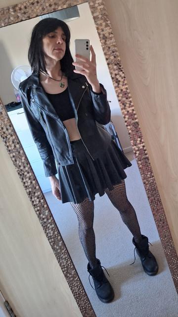 Non binary person with black hair in a biker jacket, skirt and fishnet stockings