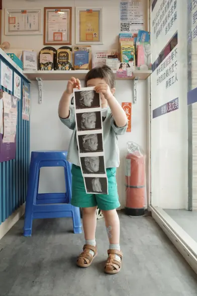 A toddler holding a set of 3D pregnancy scan printouts in front of her face