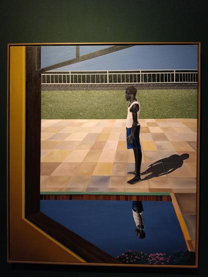 Un homme noir en short bleu et cinglet blanc se tient droit de profil au bord d'une piscine, on voit son reflet déformé par l'eau dans la piscine et son ombre projetée derrière lui par le soleil éclatant qui illumine la scène. Le carrelage est rosé.