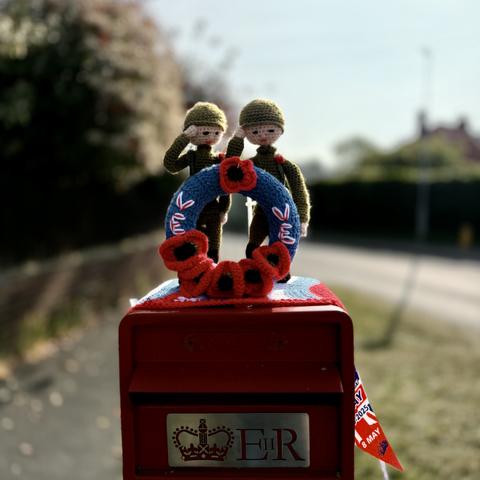 Red postbox with two knitted soldiers saluting in front of a wreath that says VE DAY on it.