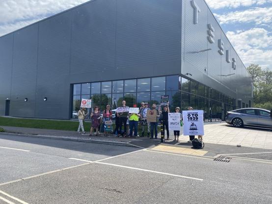 Group of people with signs outside a Tesla dealership.
