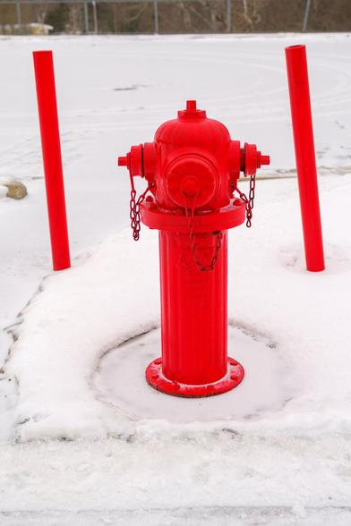 A photograph of a bright red fire hydrant standing out against the snowy landscape, flanked by two red bollards.