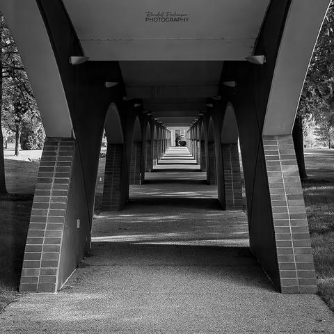 A long covered sidewalk.  Concrete and brick arches along each side support multiple arched roof sections.