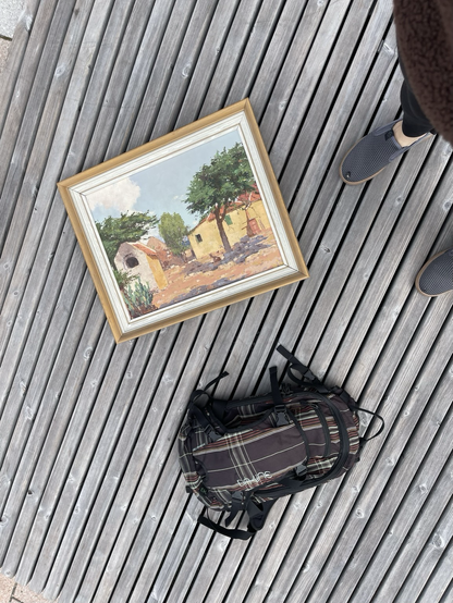 Oil painting of houses, laying on a wooden deck near a dark backpack.
