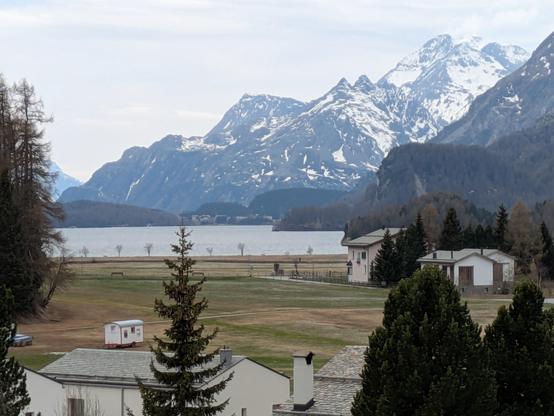 In my left, a view over the edge of town, over a flat, grassland before a big lake. Behind and to the right are mountains with the background mountain being quite well snowed on.