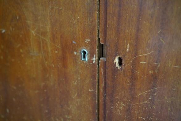 The doors of a cabinet. One door has a metal key hole cover, the other one doesn't. Both doors are well worn.