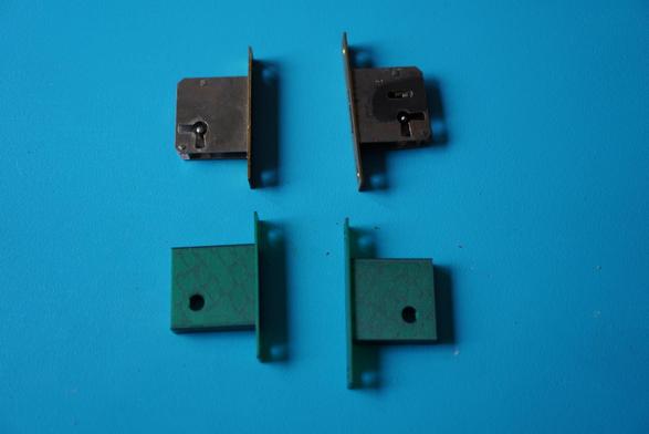 The locks taken out and next to them two 3d printed inserts of about the same shape, but without the mechanism and instead just a passthrough hole for a screw.