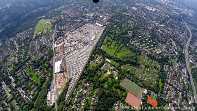 An aerial photo of Essen Altenessen Nord. The CAT Automobillogistik Essen GmbH can be seen with their big area in the middle. Living quaters with many green spaces and trees are all around.