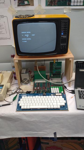 A selfbuilt keyboard with black on white XDA keys connected to a EUROCOM-1 computer. Atop is an 70s tube TV with an orange case and black front.