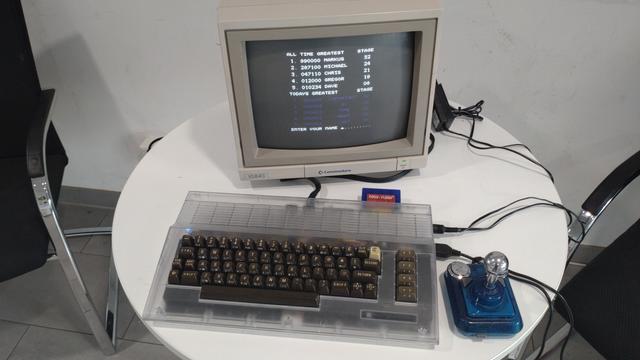 A C64 with transparent case and dark brown keys, a blue and silver joystick, and showing a game highscore.