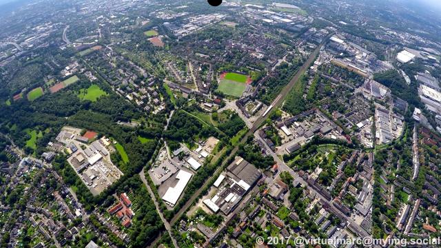 An aerial photo of the north of Essen. You can see working and living quaters between green parks and trees. A railway line is going thrugh the image.
