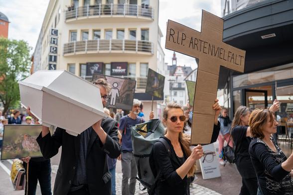Trauermarsch in der Mainzer Innenstadt. Schwarzgekleidete Menschen, im Vordergrund ein Sarg und ein Kreuz mit der Aufschrift R.I.P. Artenvielfalt