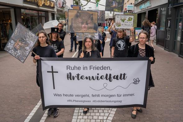 Trauermarsch in der Mainzer Innenstadt. Schwarzgekleidete Menschen, im Vordergrund Transparent mit schwarzem Rand mit der Aufschrift Ruhe in Frieden, Artenvielfalt. Was heute vergeht, fehlt morgen für immer.