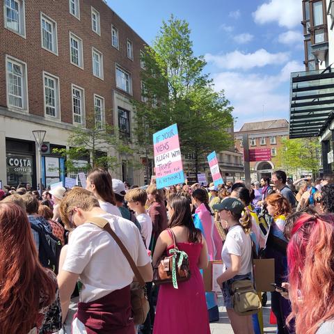 A placard held above the crowd in the colours of the trans flag saying "if your views align with Trump it's time for a rethink"