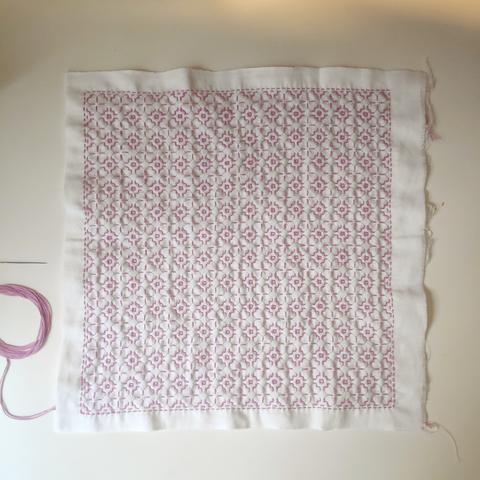 auf einem weißen Tisch ein Stück weißer Stoff mit rosa Fäden bestickt in Sashiko Technik, Muster Sakura, horizontal und vertikal ist gemacht