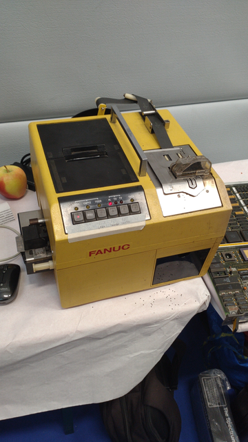 A punch tape reader and write with a yellow case, a few control buttons and a red label "FANUC".