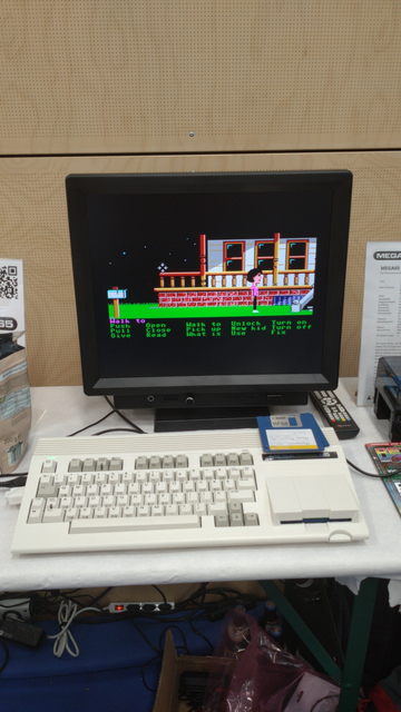 A Mega65 playing the point and click adventure Manic Mansion off a set of 3.5" floppy disks. Note the iconic magenta and green control words at the bottom of the screen:

Magenta: Walk to

Green:

Push  Open  Walk to  Unlock  Turn on
Pull  Clone  Pick up  New kid  Turn off
Give  Read  What is  Use  Fix